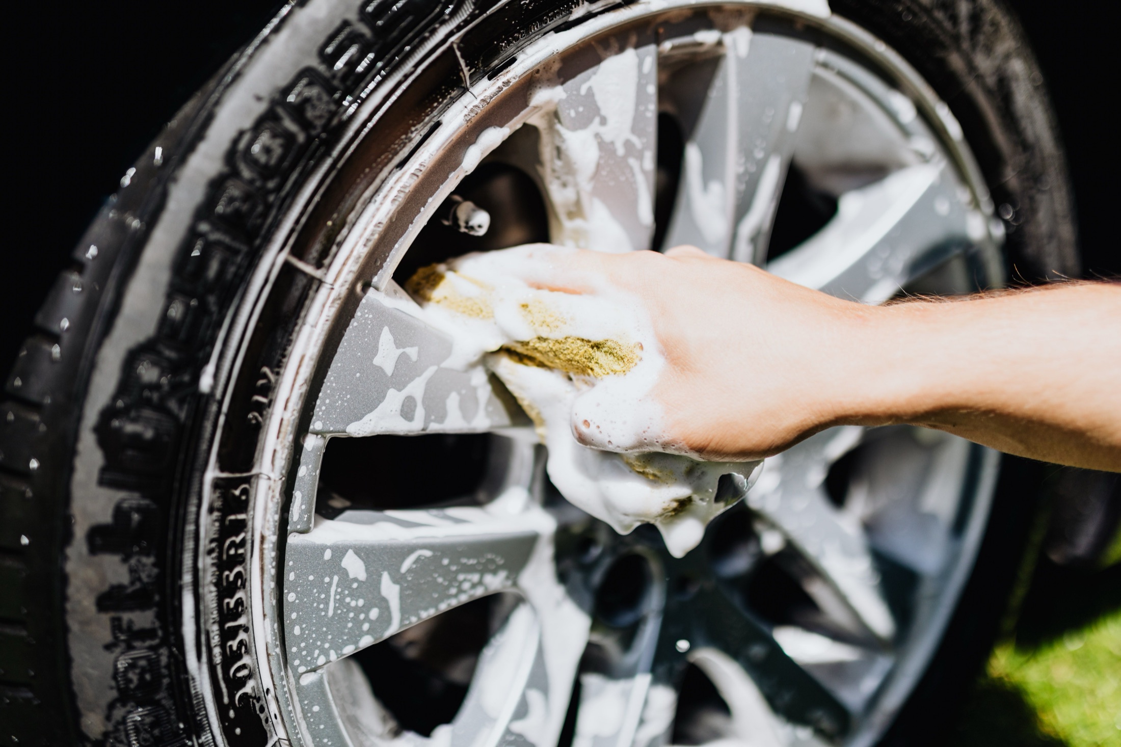 A car wheel being cleaned with foam and a detailing brush